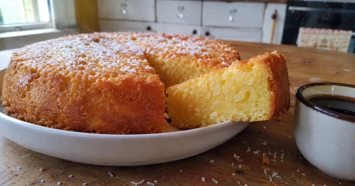 Fatia de bolo de mandioca úmido cortada sobre travessa de cerâmica branca com interior amarelo-dourado à mostra
