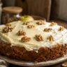 Bolo de nozes com cenoura e maçã coberto com cream cheese e nozes inteiras sobre mesa de madeira rústica