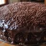 Bolo Nega Maluca sem açúcar inteiro com cobertura de ganache de chocolate e granulado, sobre mesa de madeira rústica com luz natural