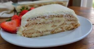 Fatia de torta alemã de leite ninho em prato branco com morangos e polvilhado de leite em pó