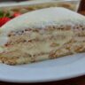 Fatia de torta alemã de leite ninho em prato branco com morangos e polvilhado de leite em pó