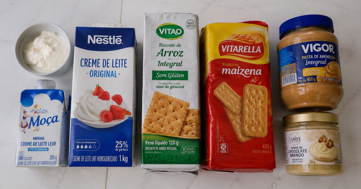 Ingredientes alternativos para torta alemã de leite ninho: biscoito sem glúten, creme de coco e pasta de amendoim sobre superfície branca