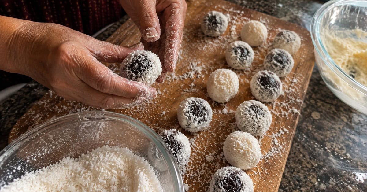 Mãos modelando bolinhas de coco e ameixa sobre tábua de madeira enfarinhada para o recheio do Bolo Olho de Sogra