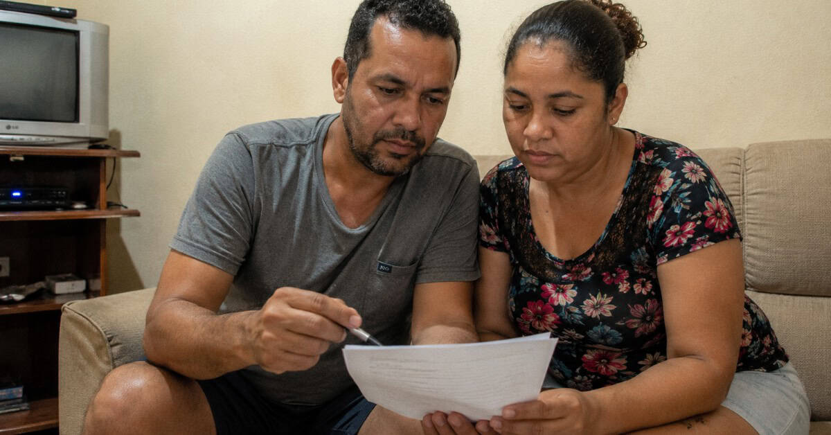 Casal sentado no sofá analisando contrato de financiamento habitacional antes de assinar pelo programa Minha Casa Minha Vida