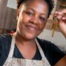 Mulher empreendedora com avental de cozinha segurando a chave da casa própria conquistada pelo programa Minha Casa Minha Vida