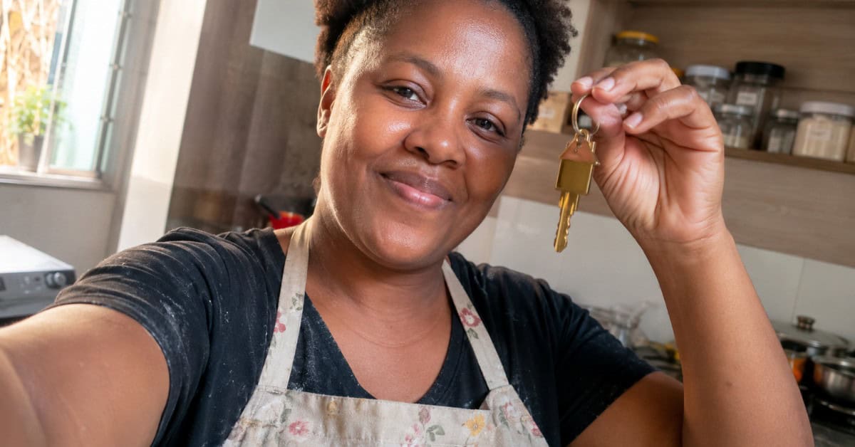 Mulher empreendedora com avental de cozinha segurando a chave da casa própria conquistada pelo programa Minha Casa Minha Vida